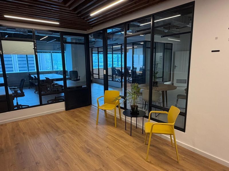 Modern office space featuring glass-partitioned meeting rooms, wood-look flooring, and recessed linear ceiling lighting, creating a professional and open work environment.