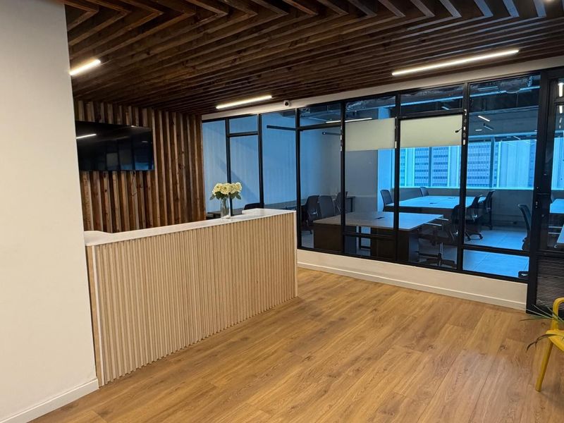 Modern office reception area featuring a custom slatted wood desk, matching timber ceiling detail, and floor-to-ceiling glass partitions overlooking an adjacent meeting room.