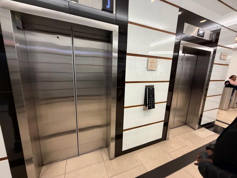 Modern office building elevator lobby featuring stainless steel lift doors, high-gloss paneling, and tiled flooring.