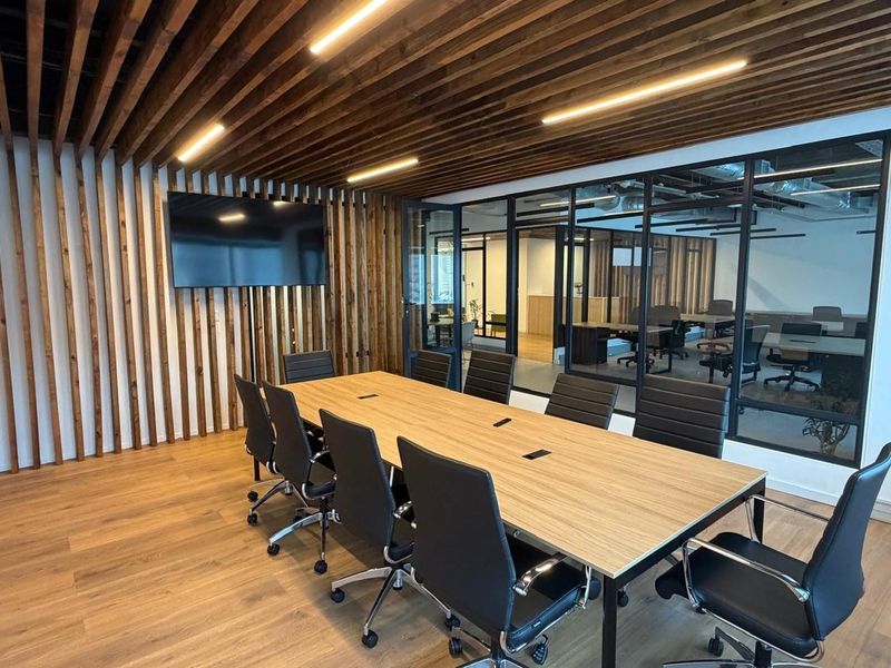 Modern office boardroom featuring a wood-slat ceiling and wall feature, glass partition walls, and integrated cable management in the conference table.