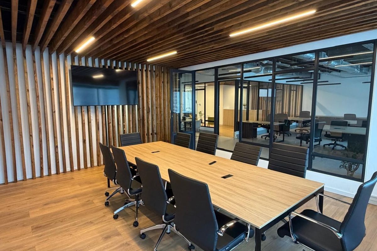 Modern office boardroom featuring a wood-slat ceiling and wall feature, glass partition walls, and integrated cable management in the conference table.