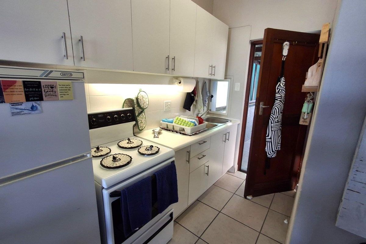 Compact kitchen featuring white cabinetry, tiled flooring, and a freestanding stove with an integrated extractor fan.