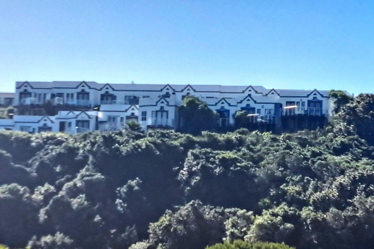 A distant exterior view of a multi-unit apartment complex featuring gabled rooflines and balconies, set against a natural landscape.