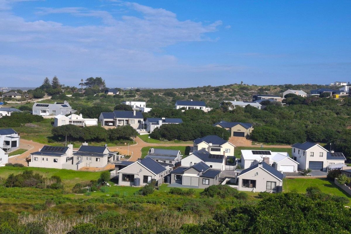 An elevated aerial view of a residential estate featuring modern homes with pitched roofs, solar panels, and landscaped surroundings.