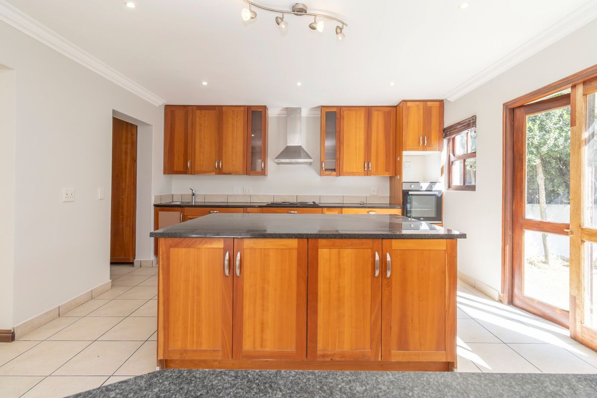 A spacious kitchen featuring wooden cabinetry, granite countertops, a central island, and built-in appliances, with direct access to the outdoor area.