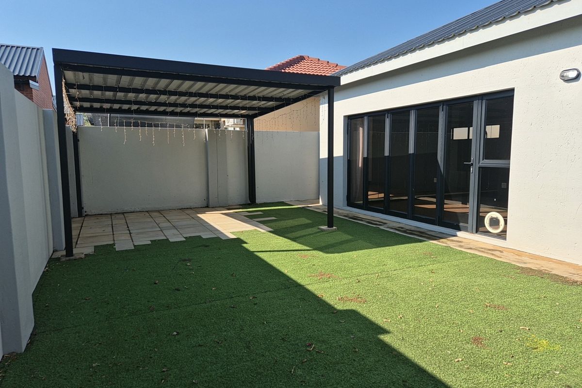 A well-maintained rear exterior featuring a covered patio area, artificial lawn, and modern black-framed bi-fold doors leading into the home.