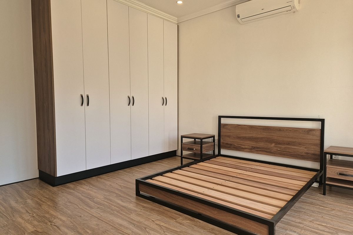 A well-maintained bedroom featuring modern laminate flooring, a large built-in wardrobe, and a wall-mounted split-system air conditioning unit.