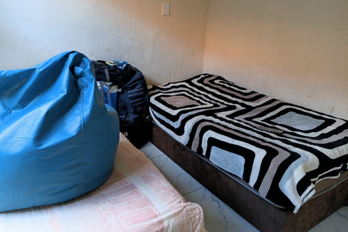 A bedroom featuring tiled flooring and plain wall finishes, currently utilized as a sleeping space.