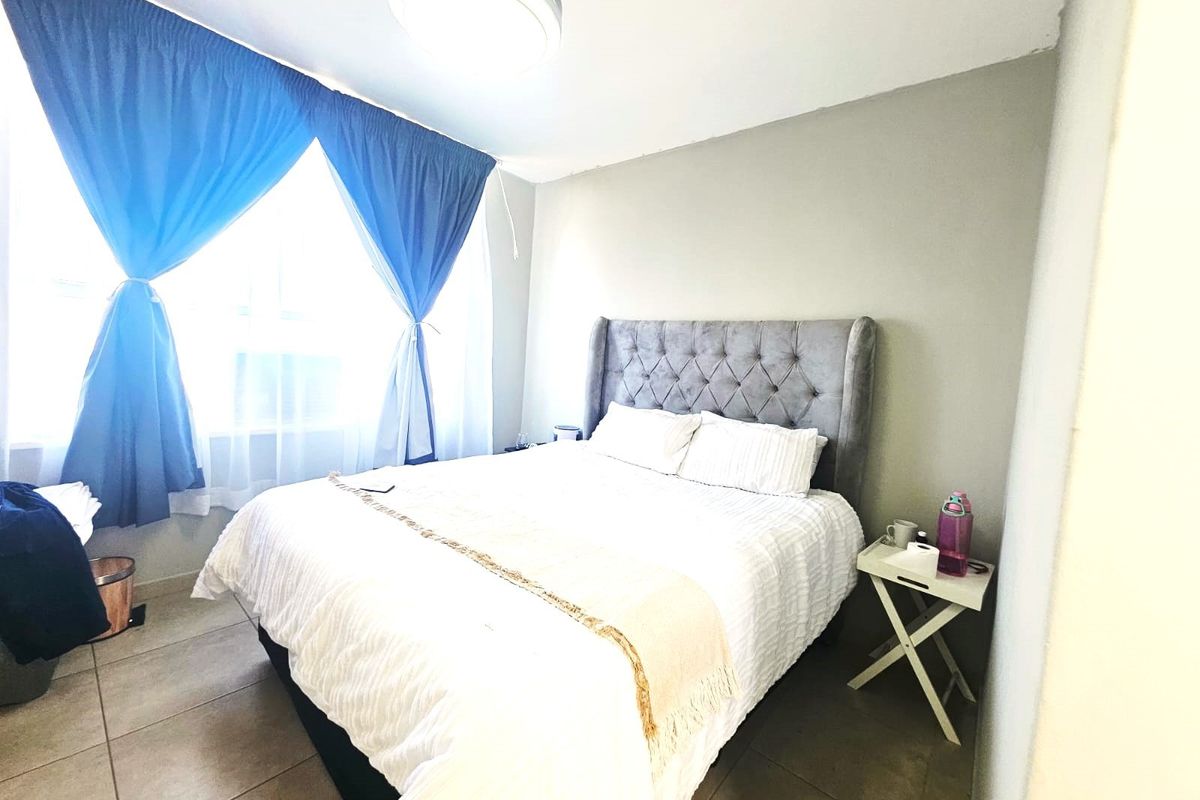 A bedroom featuring tiled flooring and a large window with curtains, providing natural light to the space.