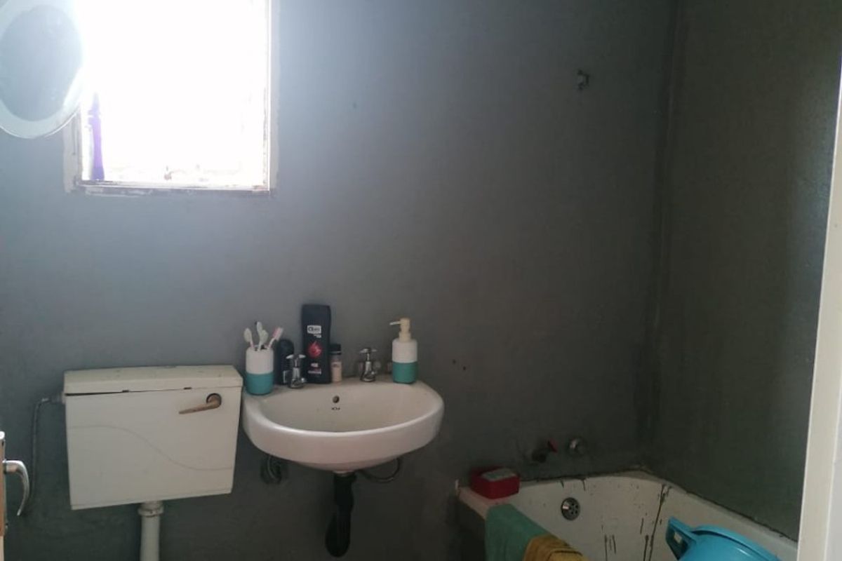A compact bathroom featuring a standard bathtub, wall-mounted basin, and toilet, requiring cosmetic updates to improve the overall finish and aesthetic.
