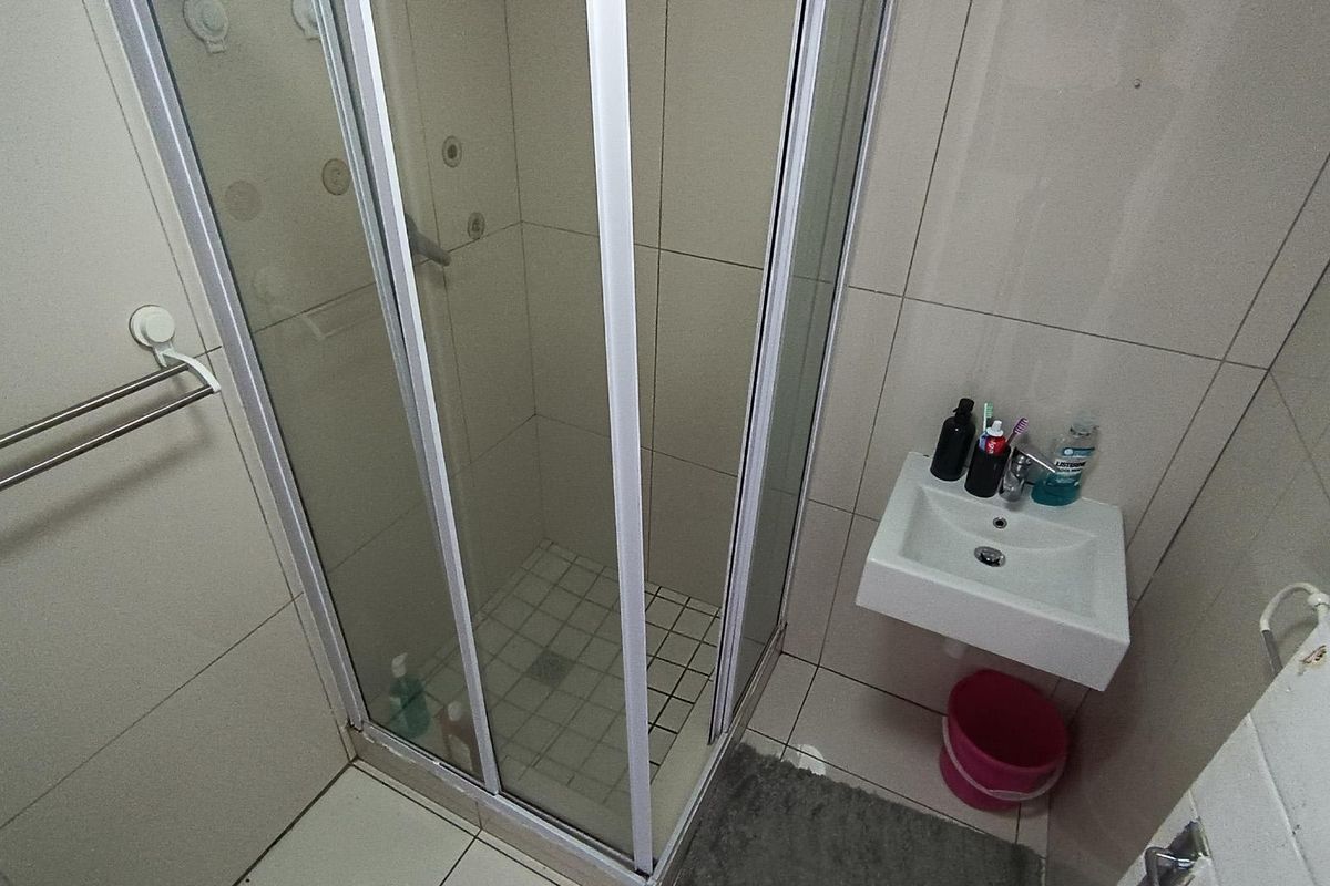 Compact bathroom featuring a corner shower enclosure with glass doors and a wall-mounted basin with tiled walls and flooring.