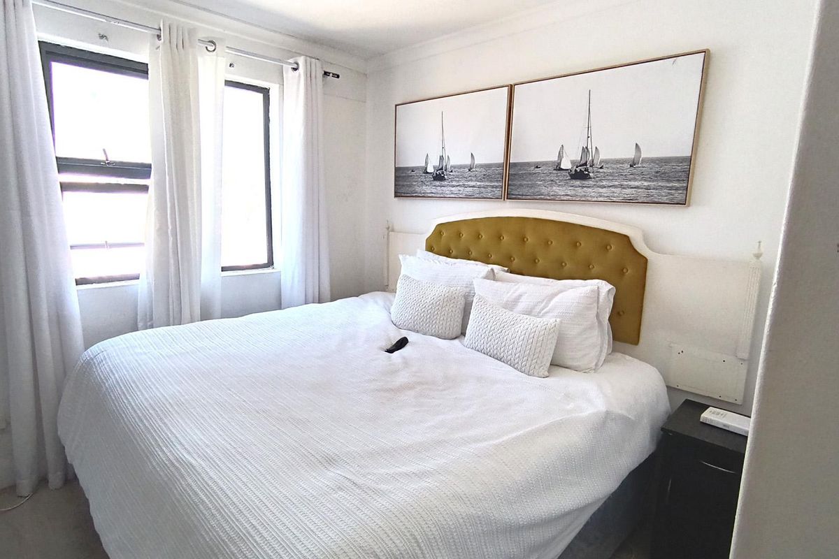 A well-lit bedroom featuring neutral walls, carpeted flooring, and large windows that provide natural light.