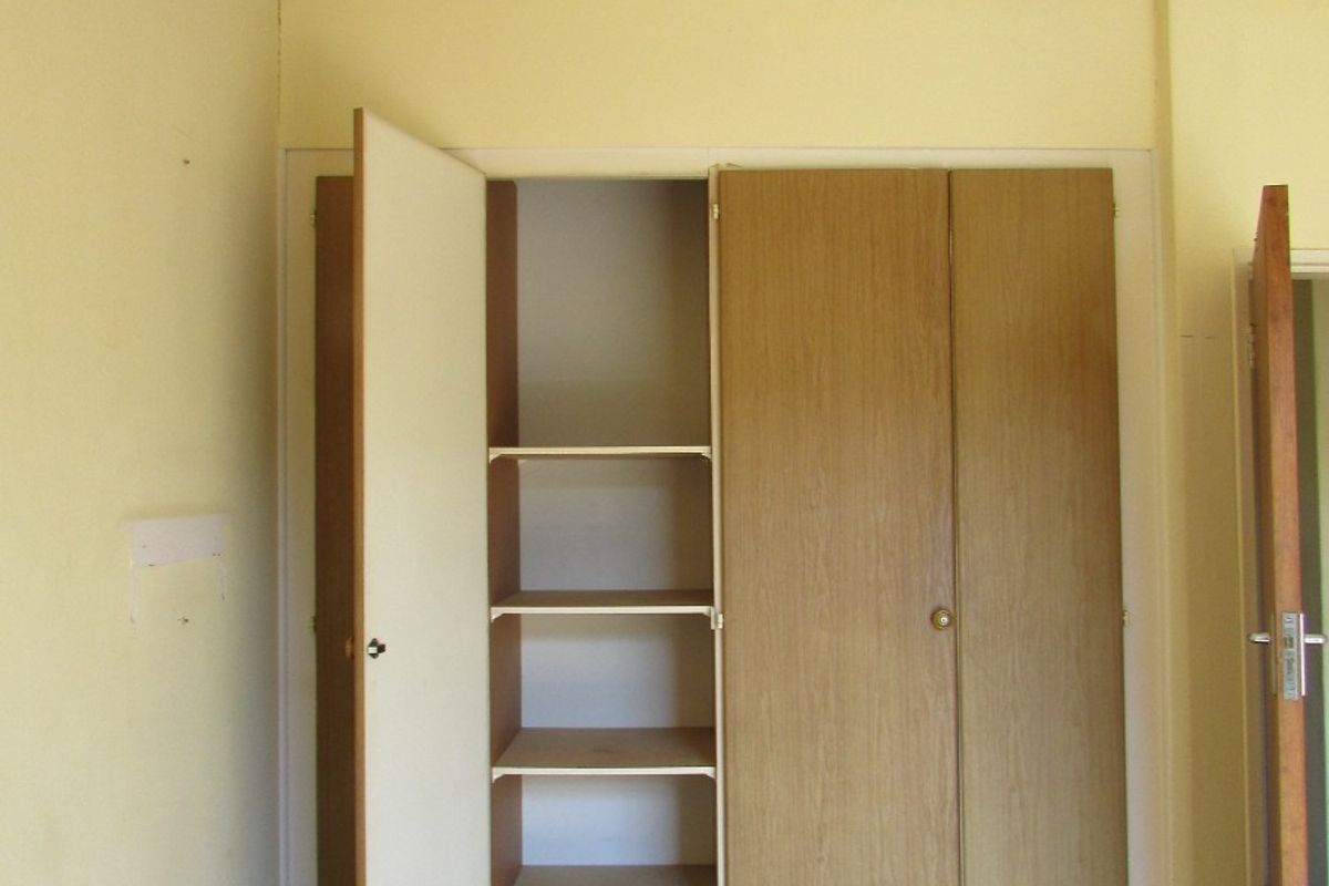 A bedroom featuring built-in wooden cupboards with shelving and neutral wall finishes.