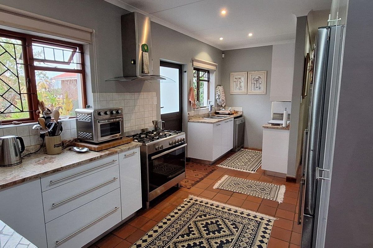 A functional kitchen featuring white cabinetry, stone-look countertops, a stainless steel gas stove with extractor fan, and terracotta floor tiles.