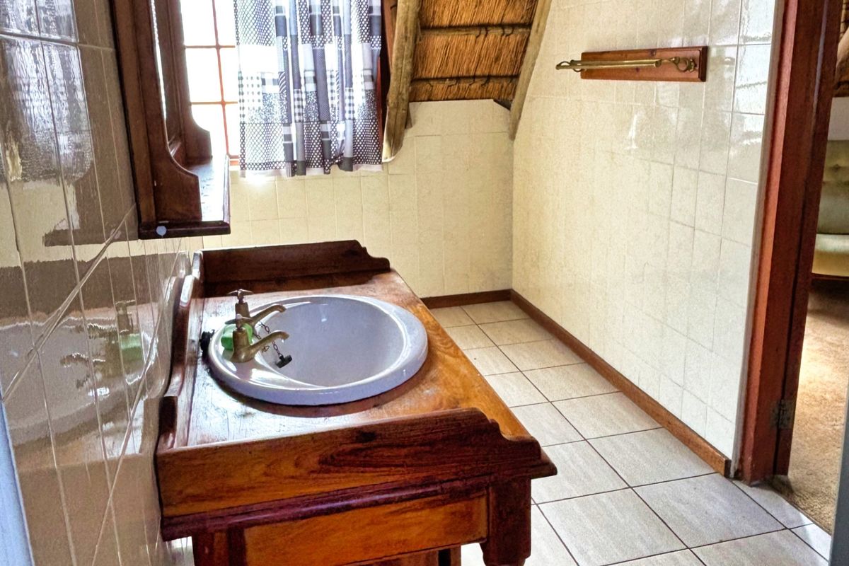 A bathroom featuring a wooden vanity with a drop-in basin, tiled walls and flooring, and a distinctive thatched roof ceiling detail.