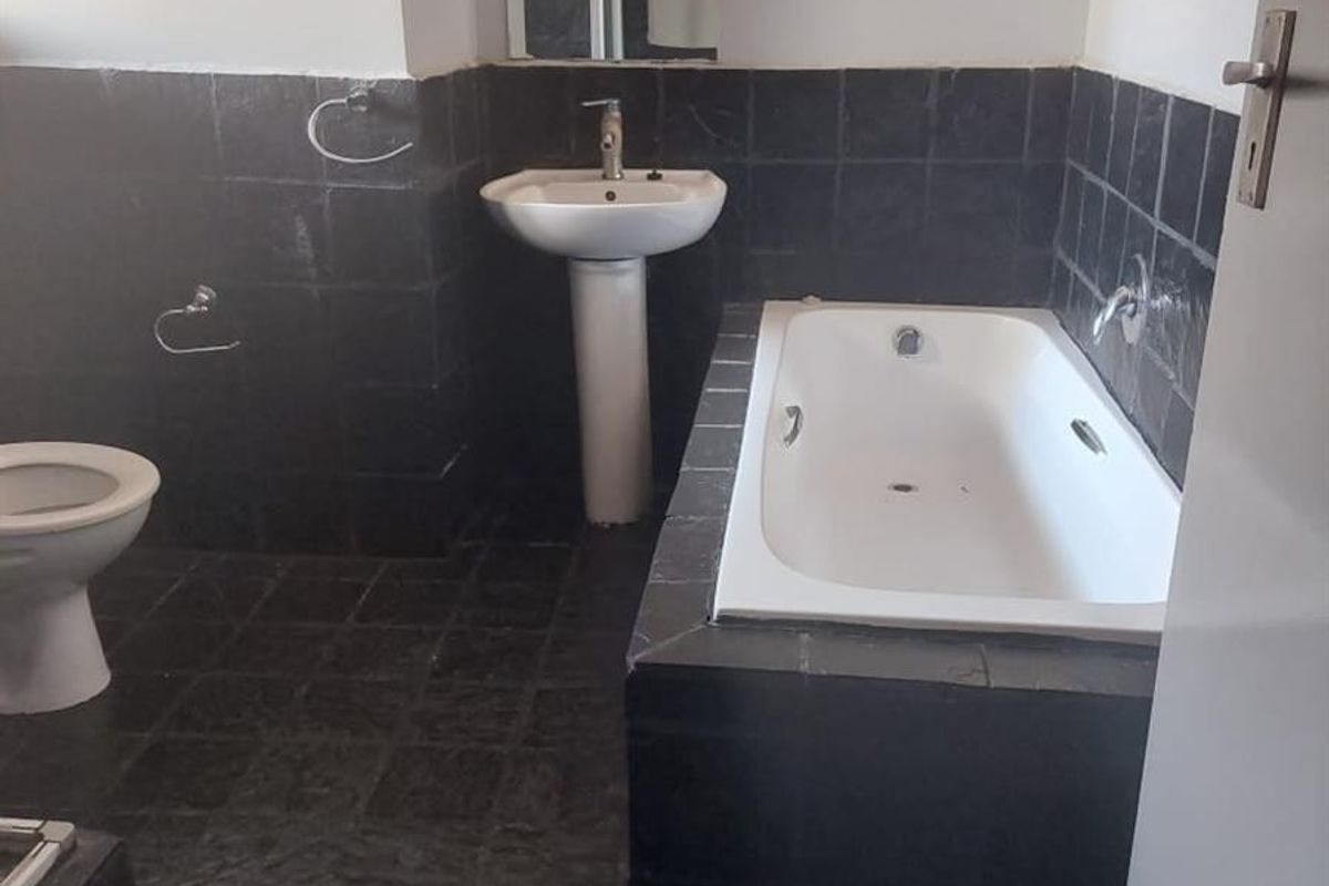 A functional bathroom featuring a pedestal basin, built-in bathtub, and toilet with dark tiled finishes throughout.