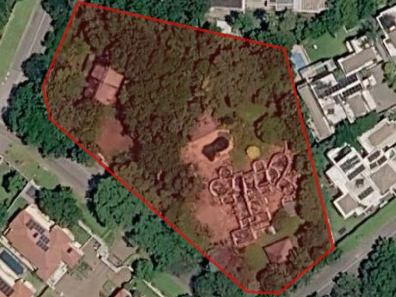 An aerial view of a residential property plot featuring mature trees, existing structures, and a swimming pool within a defined boundary.