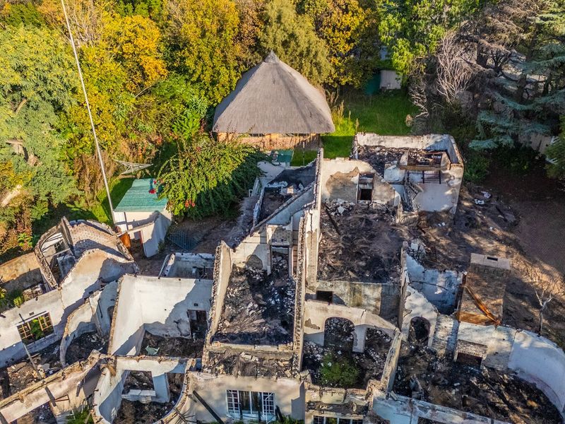 Aerial view of a residential property showing a severely fire-damaged structure with collapsed roofing and extensive debris throughout the site.