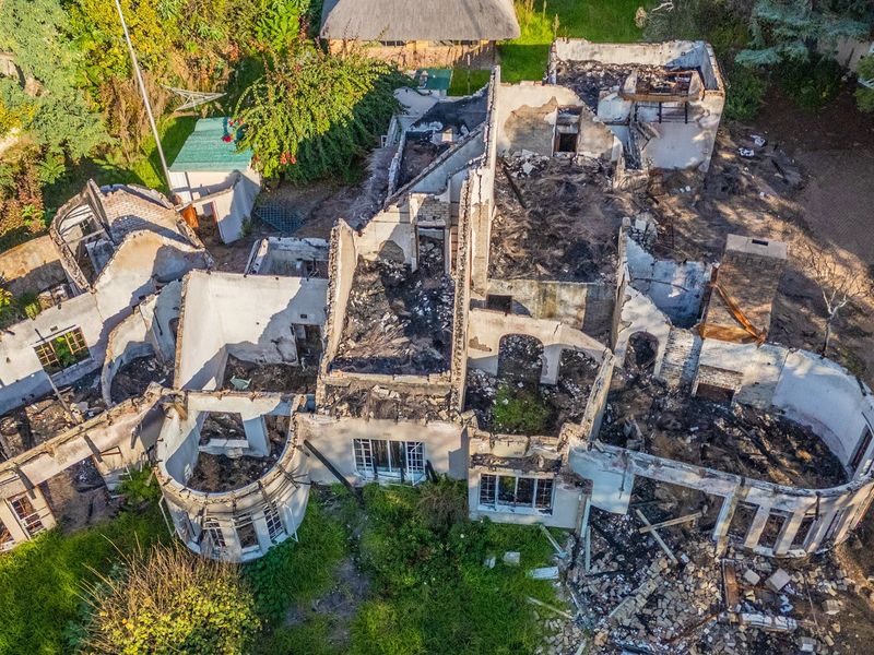 Aerial view of a residential property showing extensive fire damage, with the roof structure collapsed and walls severely charred throughout the building footprint.