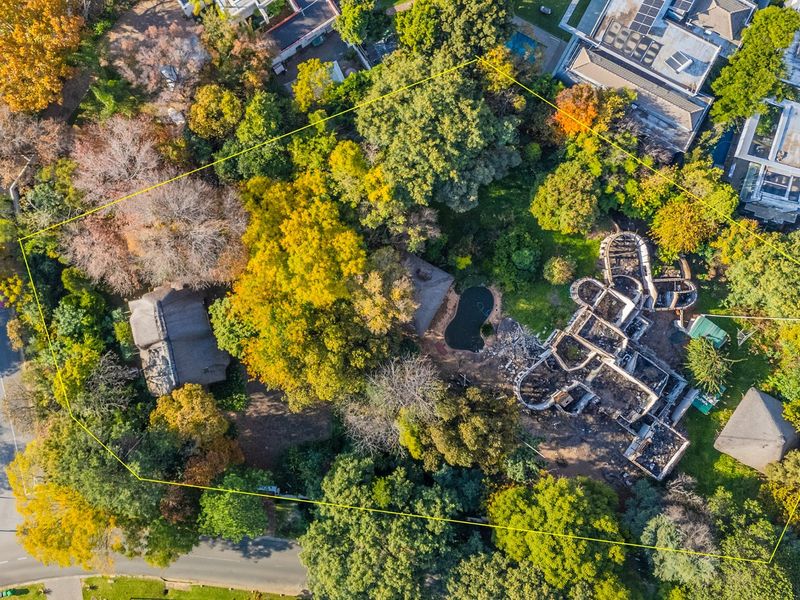 Aerial view of a residential plot featuring mature trees, a swimming pool, and the remains of a fire-damaged structure.