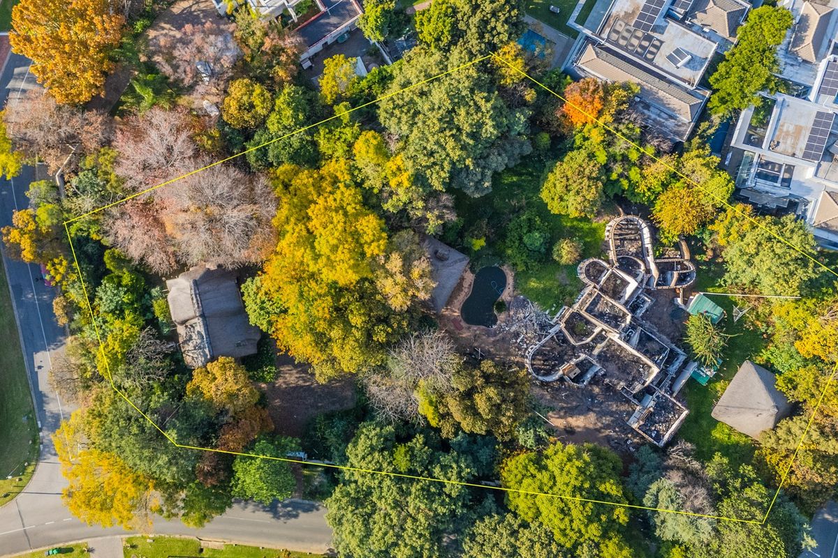 Aerial view of a residential plot featuring mature trees, a swimming pool, and the remains of a fire-damaged structure.