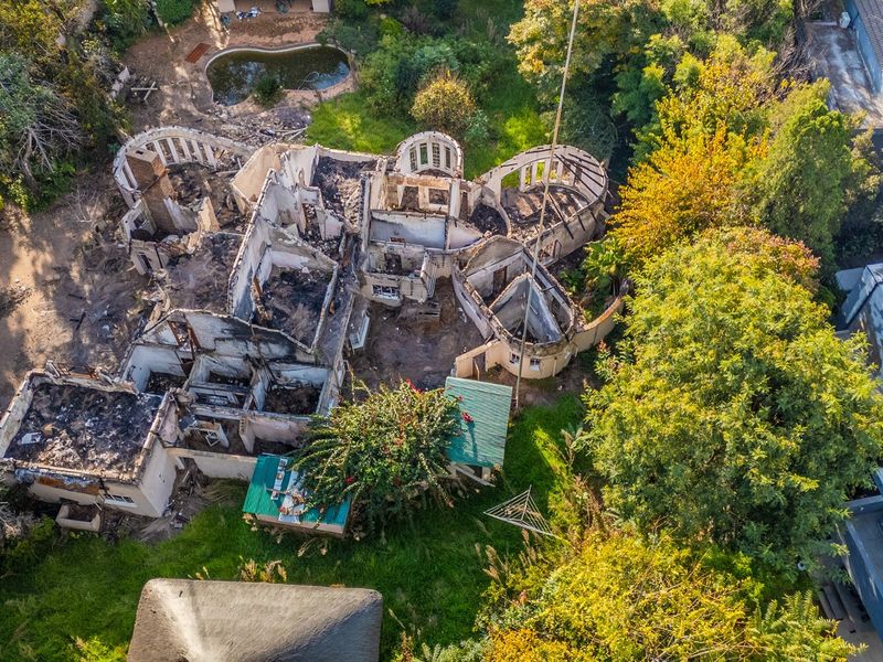 Aerial view of a residential property showing significant fire damage and structural destruction to the main dwelling and surrounding grounds.