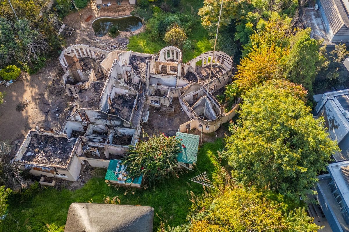 Aerial view of a residential property showing significant fire damage and structural destruction to the main dwelling and surrounding grounds.