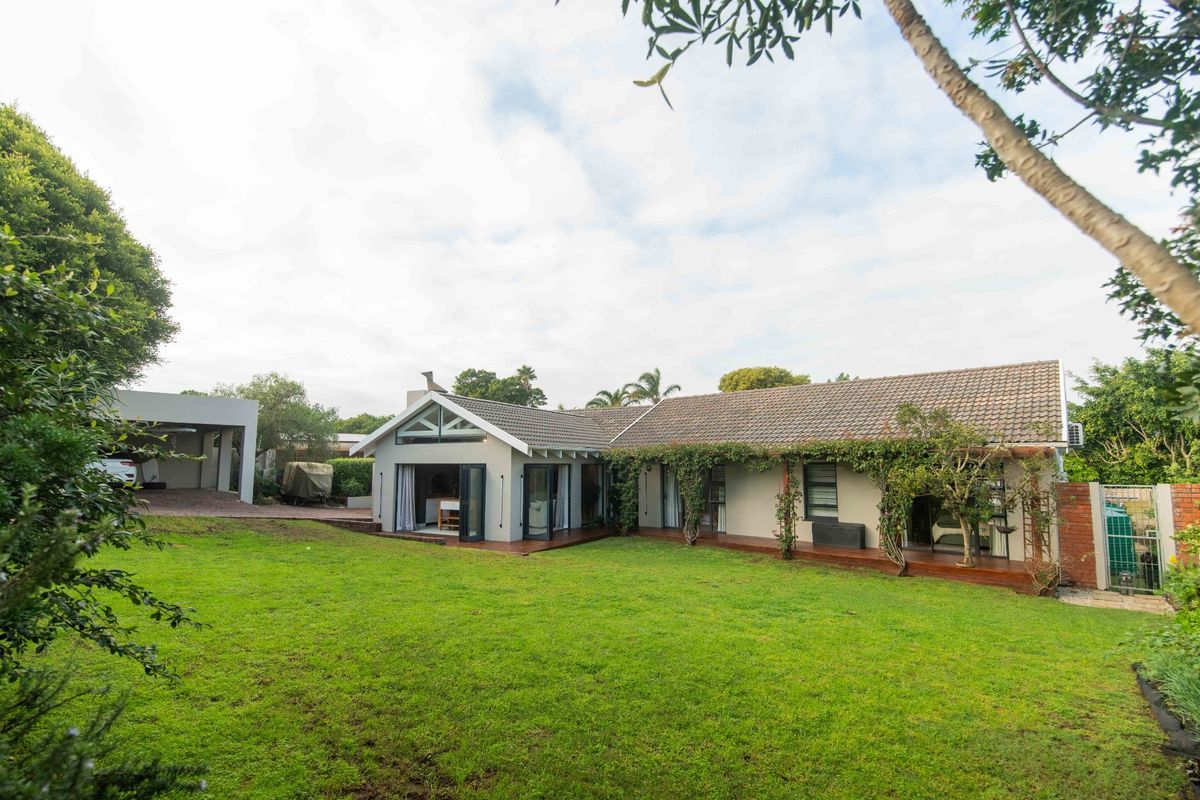 Rear view of the property featuring a spacious lawn, timber decking, and a modern extension with bi-fold doors opening to the garden.