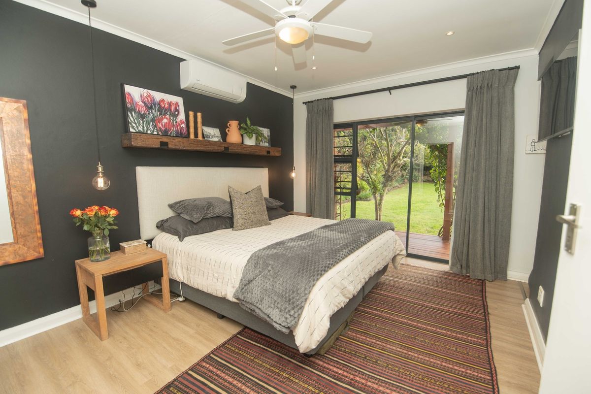 A well-maintained bedroom featuring a dark accent wall, ceiling fan, air conditioning unit, and sliding glass doors providing direct access to the garden.