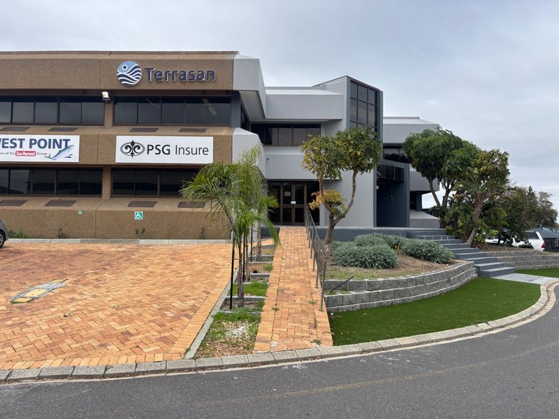 Front exterior view of a multi-story commercial office building featuring paved access, landscaped garden areas, and prominent corporate signage.