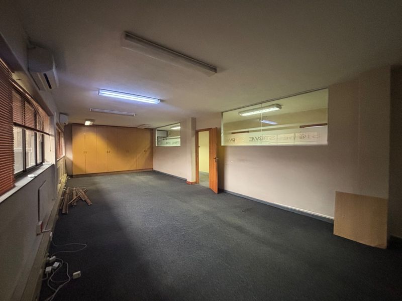 Spacious empty office area featuring built-in storage cabinetry, internal glass partitions, fluorescent lighting, and air conditioning, suitable for a professional workspace.