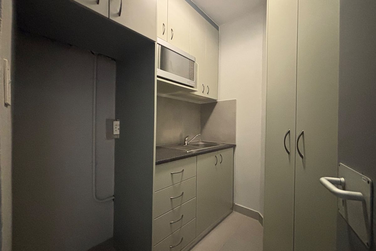 A compact kitchenette featuring built-in cabinetry, a stainless steel sink, integrated microwave, and additional full-height storage cupboards.