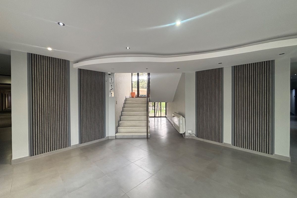 Modern office building entrance lobby featuring contemporary slatted timber wall paneling, tiled flooring, and a distinctive curved bulkhead ceiling design.