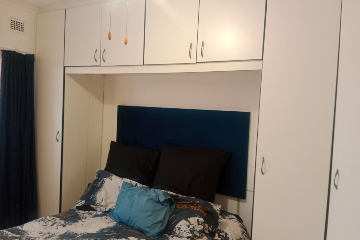 A bedroom featuring extensive built-in white cabinetry and overhead storage units surrounding the bed area.