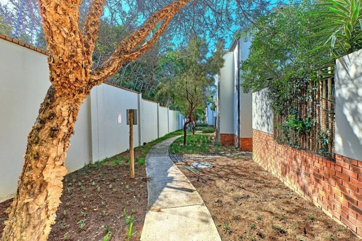 A rear exterior view of the apartment complex featuring a concrete pathway, boundary walls, and established garden landscaping.