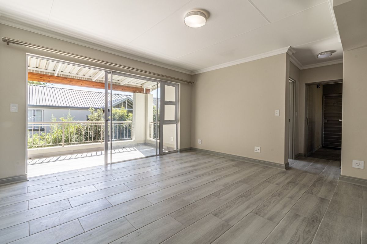 Bright and spacious living area featuring modern wood-look tile flooring, neutral walls, and direct access to a private balcony through large sliding glass doors.