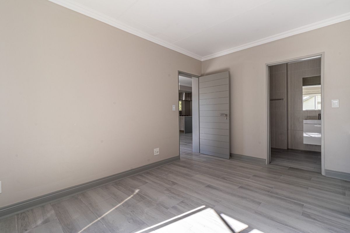 A bright, empty bedroom featuring modern grey laminate flooring, neutral wall tones, and direct access to an en-suite bathroom.