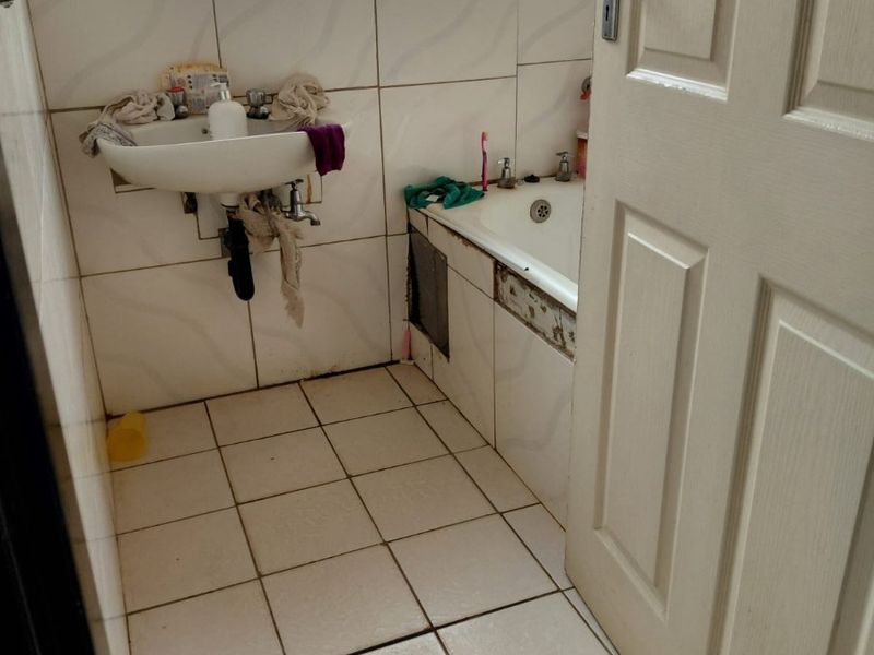 A compact bathroom featuring a wall-mounted basin and built-in bathtub, requiring maintenance and cosmetic updates to the tiling and fixtures.