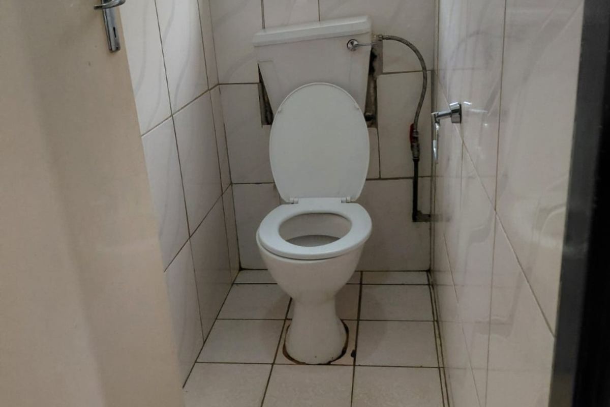 A small, functional bathroom featuring ceramic wall and floor tiles, a standard toilet, and a window with security bars.