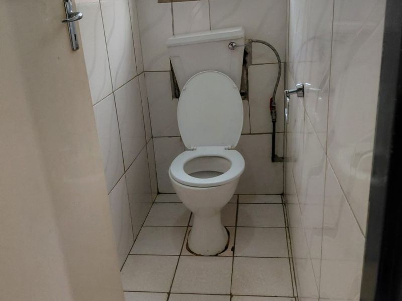 A small, functional bathroom featuring ceramic wall and floor tiles, a standard toilet, and a window with security bars.