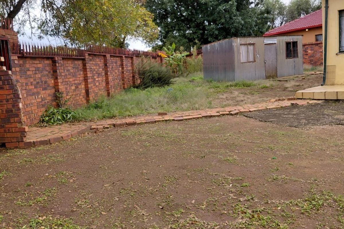 A spacious rear garden area featuring a brick boundary wall, a metal storage shed, and a paved walkway leading to the main house structure.