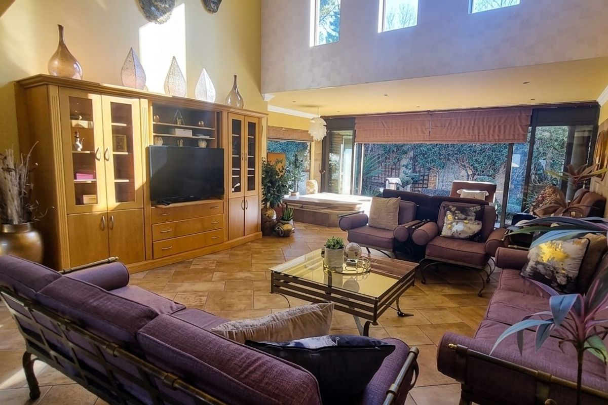 Spacious living room featuring high ceilings, large windows, tiled flooring, and a built-in wooden entertainment unit with direct access to the outdoor area.