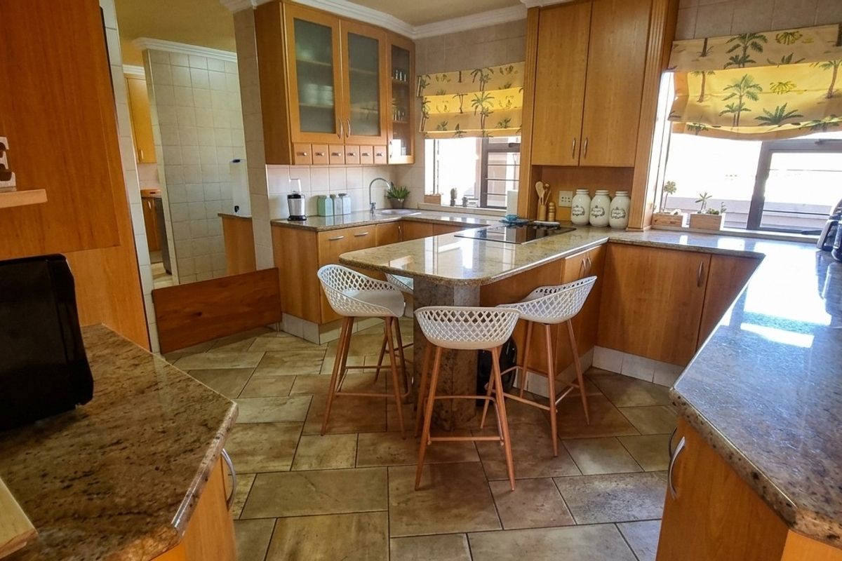 A functional kitchen featuring wooden cabinetry, granite countertops, a central breakfast bar, and tiled flooring, offering a warm and traditional aesthetic.