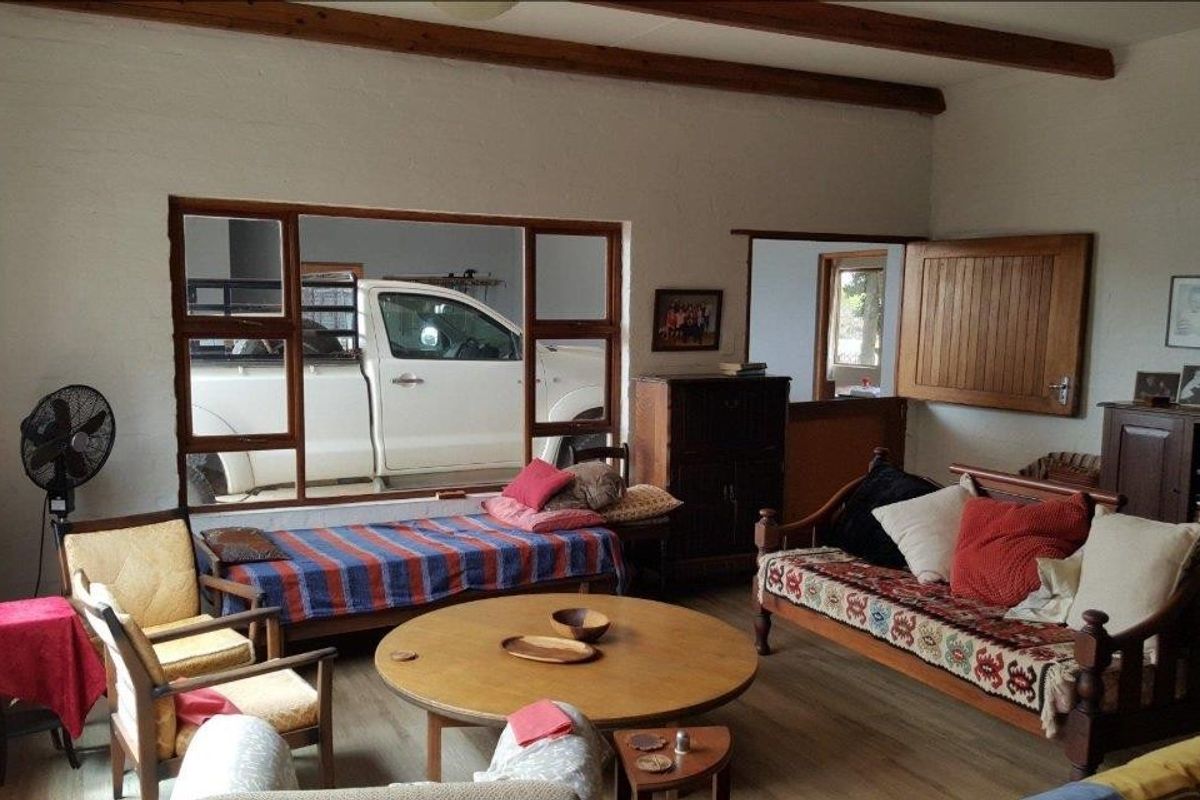 A rustic living room featuring exposed timber ceiling beams, large windows, and a stable-style door leading to an adjacent space.