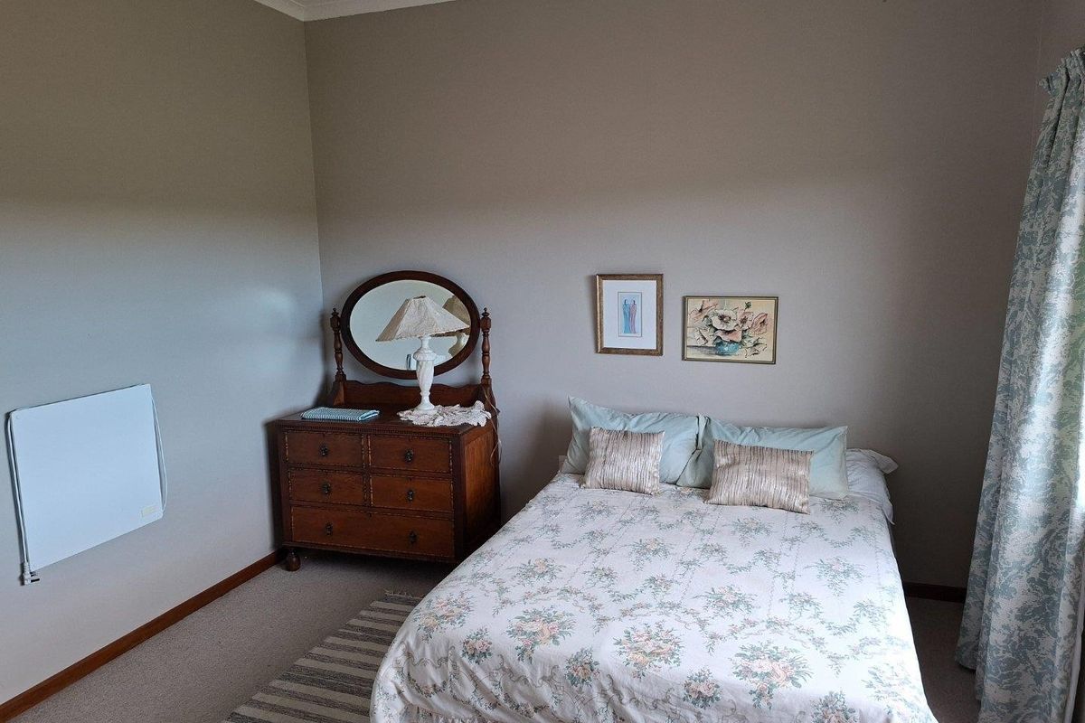 A well-maintained bedroom featuring neutral wall tones, carpeted flooring, and a wall-mounted electric panel heater.