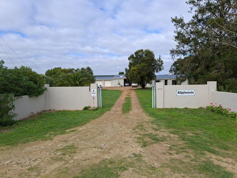 Entrance view of the Klipfontein farm property, featuring a gated access point, gravel driveway, and main building structure with garage facilities.