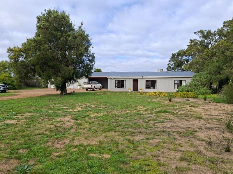 A single-story farm residence featuring a neutral facade, corrugated metal roof, and an attached garage, set within a spacious, open rural landscape.