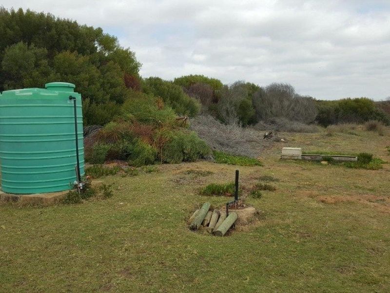 A rural farm landscape featuring a large green water storage tank and exposed irrigation or utility piping set within a natural field.