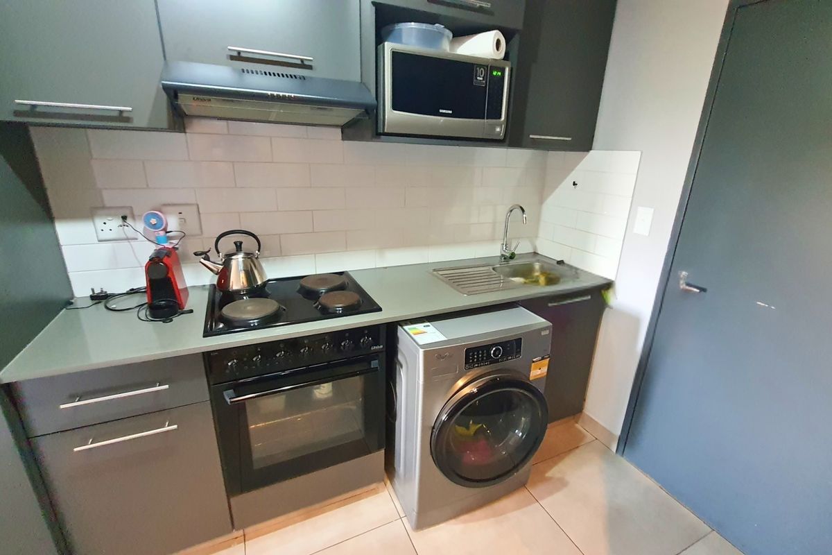 Compact kitchen featuring modern grey cabinetry, subway tile backsplash, built-in electric oven and hob, extractor fan, and integrated space for a washing machine.