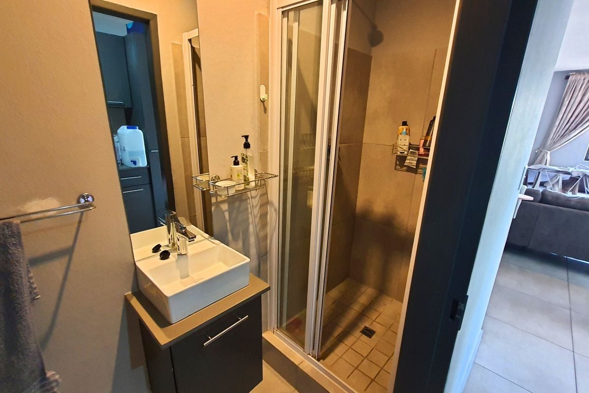 A compact bathroom featuring a modern vessel sink vanity, a glass-enclosed shower, and neutral wall tiling.